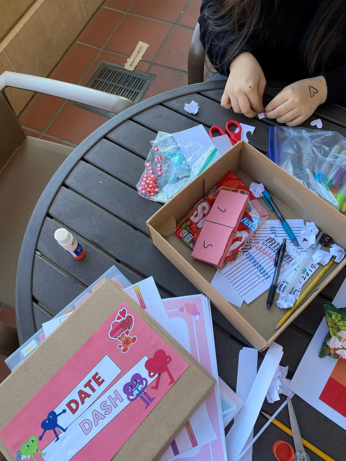 A teammate cutting out paper hearts at a table covered in craft supplies, the Date Dash box, heart counters and score sheets