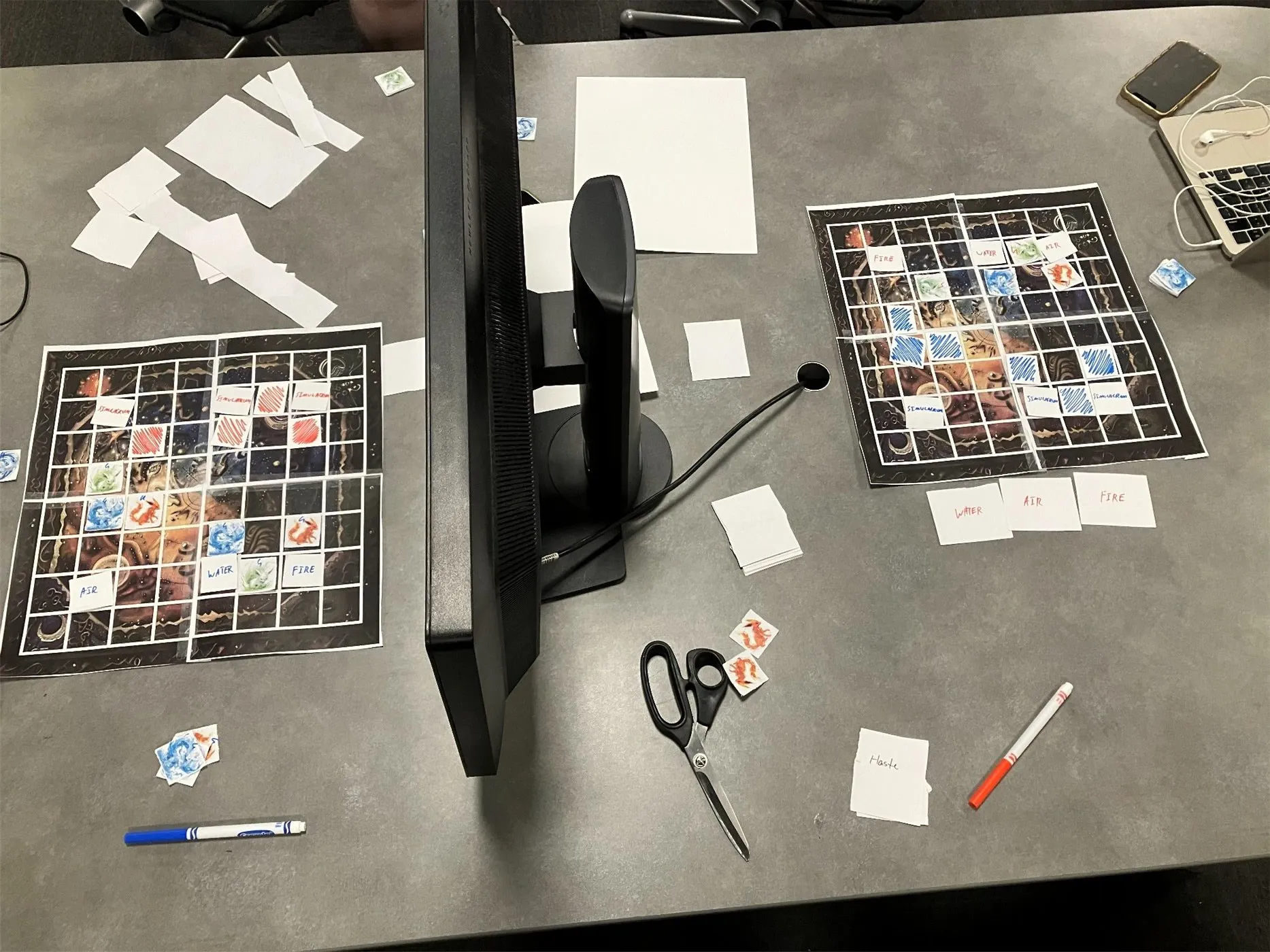 Two 8x8 boards on a table with a computer monitor between them as a divider, covered in paper tokens, hand-written Air/Water/Fire command cards and Simulacrum pieces