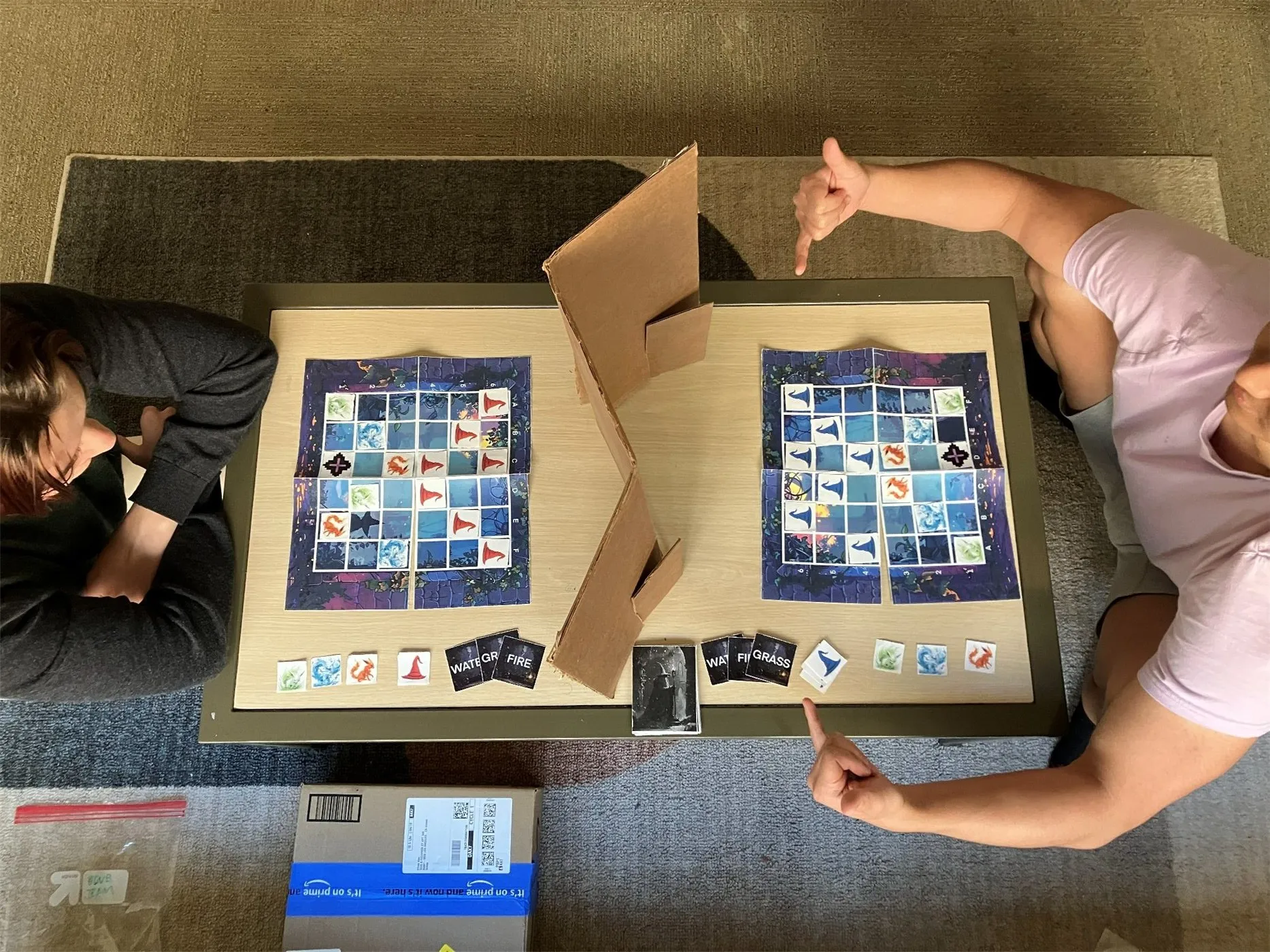 A top-down view of two players' boards where the enemy positions are marked with red and blue wizard-hat tiles