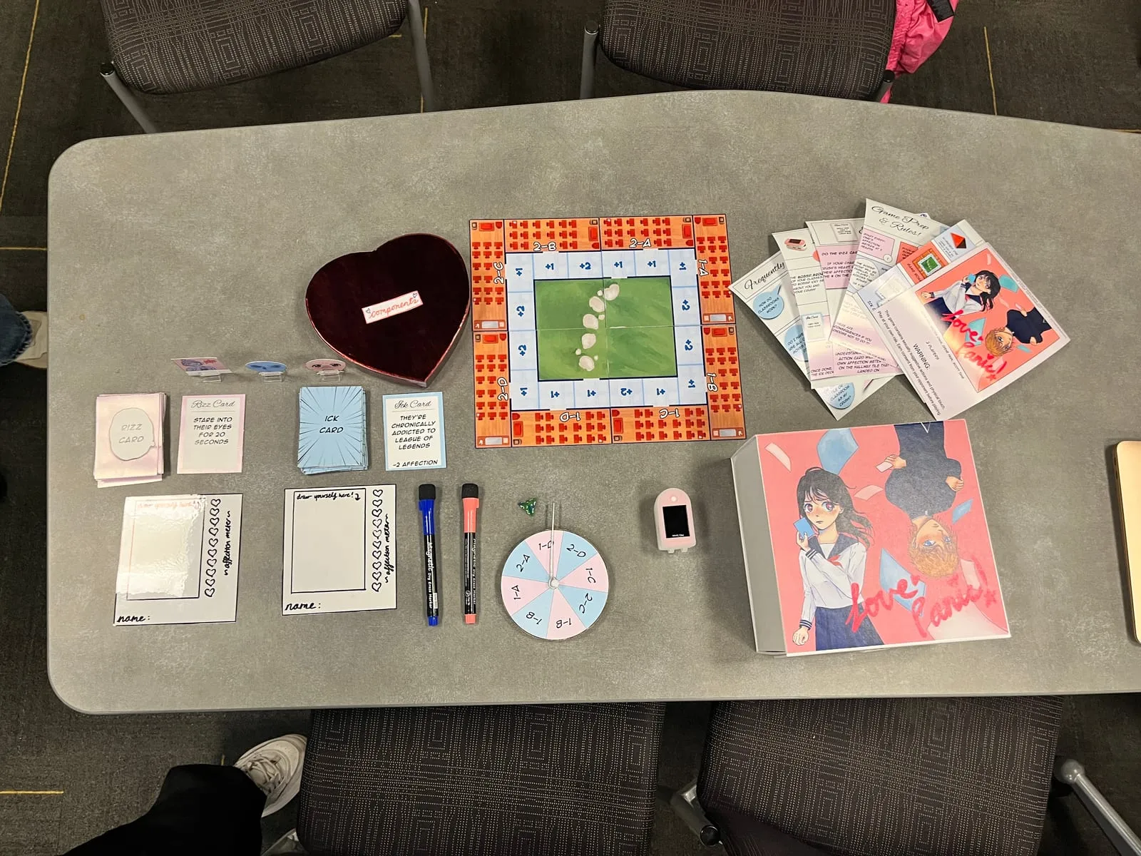 The full Love Panic set on a table: heart-shaped box, Rizz and Ick cards, dry-erase profile cards, board, spinner, heart rate monitor, rulebook and the boxed game
